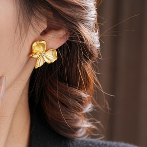 Macro view of gold flower earrings with matte finish and center zircon on a model