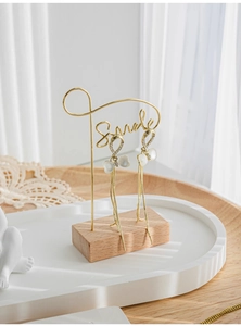 Golden tassel earrings with white heart pendant hanging on a metal display stand