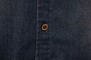 Macro shot of dark blue denim shirt detail with brown wood-textured button and neat stitching