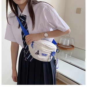 Detail showing white canvas crossbody bag with blue woven strap and fashion pendant
