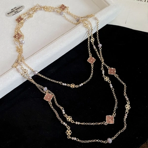 Detail of a gold clover long necklace with pink-brown petals and purple beads