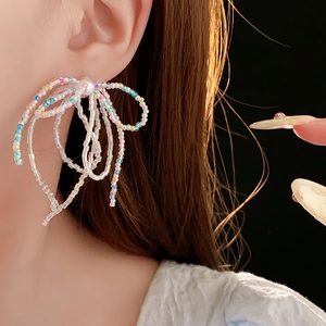 Detail of colorful beaded bow earrings with white pearl accent worn by model