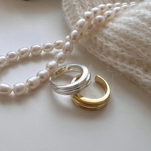 Close-up of stacked silver and gold irregular open rings with elegant pearl necklace