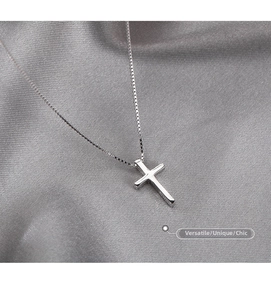 Macro detail of silver cross pendant on fine box chain over gray silk background