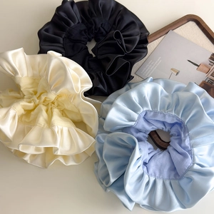 Close-up of three oversized satin ruffles in black, beige, and light blue on a tray