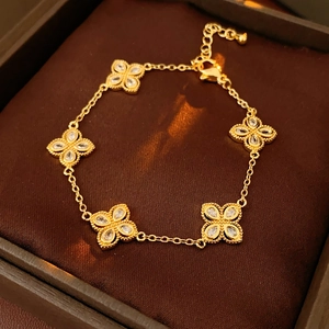 Close-up of golden clover bracelet with white zircon pendants on brown velvet box