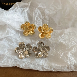 Detailed macro view of gold and silver metallic flower stud earrings on textured background