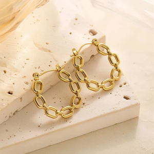 Macro d'une boucle d'oreille en chaîne dorée 18k en acier inoxydable sur pierre beige