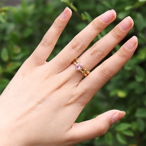 Vue détaillée d'une bague dorée à double rangée avec une pierre rose sur le doigt