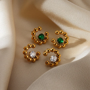 Detail of C-shaped gold-plated earrings with green and white round gemstones on silk