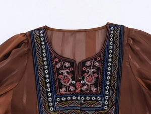 Détails d'une robe bohème marron avec broderies, manches transparentes et trois boutons fins