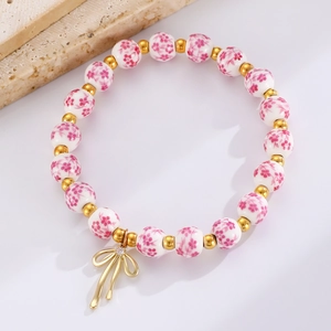 Dettaglio di perline in ceramica floreale e ciondolo a fiocco dorato su bracciale