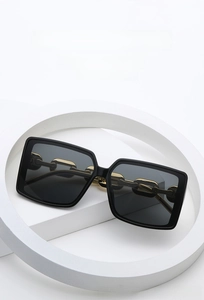 Detailed view of square sunglasses with black frames and decorative gold chain temples