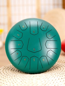 Top view of dark green steel tongue drum with gold numbered scales on woven mat