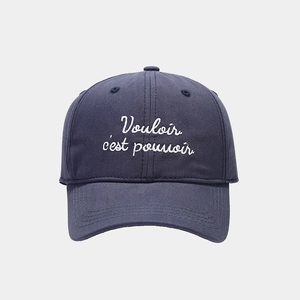 Detailed close-up of navy blue cotton baseball cap with white Vouloir c'est pouvoir embroidery