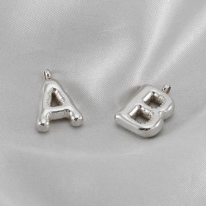 Macro detail of silver bubble letter A and B pendants on a smooth silk fabric background