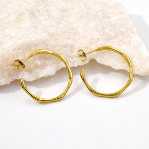 Detail view of irregular wavy gold hoop earrings on a minimalist white background