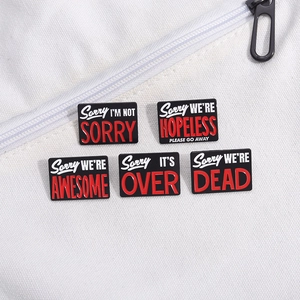 Set of 5 black enamel pins with sarcastic red and white text on a canvas bag background