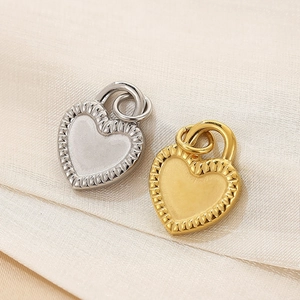 Detail of gold and silver heart pendants with textured edges on a beige fabric background