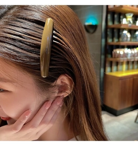 Detail view of a long curved tortoiseshell finish hair comb clip on a brunette woman