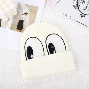Cute off-white knit beanie for kids with large cartoon eyes on a lifestyle background