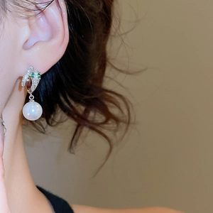 Detail of a 14K gold-plated earring with emerald gems and a white freshwater pearl