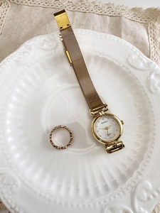 Detail of vintage gold quartz watch with crystal indices and woven ring on ceramic plate