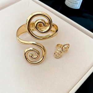 Close-up of golden spiral bangle and ring set on a cream velvet jewelry display tray