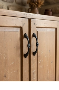 Close-up of black cast iron cabinet handles with vintage floral relief on wood doors
