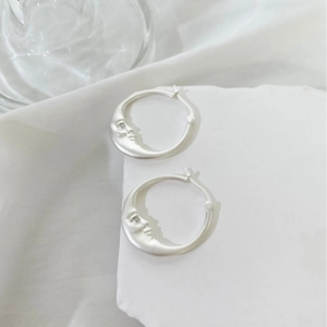 Matte silver crescent moon hoop earrings with zircon accents on white stone display