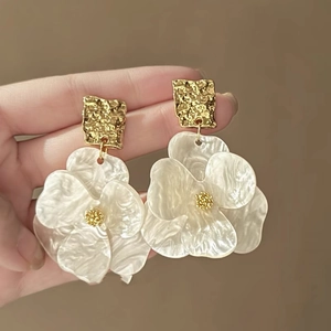 Detail of hand-held gold square metal and pearlescent white flower drop earrings