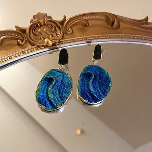 Macro shot of dark blue resin drop earrings with gold edges on a vintage mirror