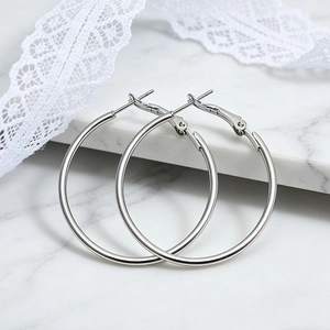 Macro view of silver chunky hoop earrings with hinged clasp on white marble surface