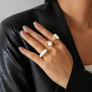 Close-up of golden layered rings with baroque pearls worn on a finger against black leather