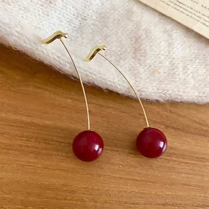 Elegant cherry drop earrings with gold hooks and deep red resin beads on a textured surface