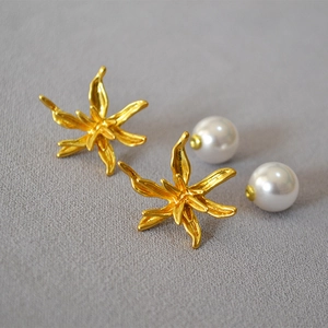 Artistic gold flower earrings with large white pearls on a textured background
