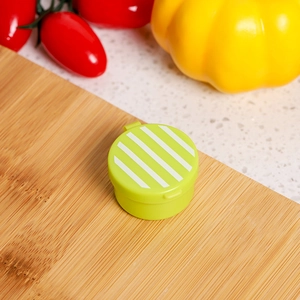 Mini green plastic sauce container with white stripe lid on a bamboo board in a kitchen