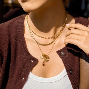 Detail of layered gold stainless steel necklace with daisy, heart and bar charms
