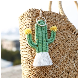 Macro detail of handmade green beaded cactus keychain with white tassel on straw bag