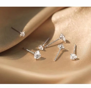 Macro shot of 999 silver heart zircon stud earrings on champagne silk fabric background