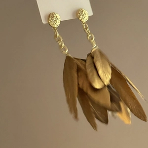 Detail of bohemian gold feather earrings with textured metal studs and long brown tassels