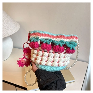 Detail of a pink and blue crochet bucket bag with pearl handle held by a model