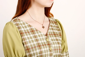 Detailed view of rose gold Tree of Life pendant necklace worn on a green plaid dress