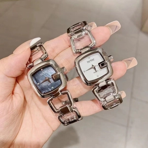 Detail showing two square quartz watches with blue and white dials and silver hollow bands