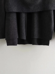Detail of multi-layered hem on dark gray knit jacket with wool-like fabric texture