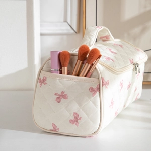 Detail of white quilted makeup bag featuring pink bow patterns and front pocket utility