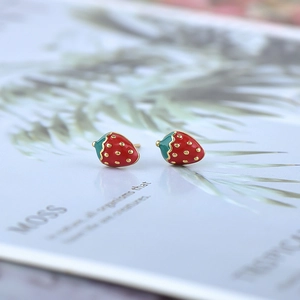 Close-up of cute strawberry stud earrings with red enamel finish and golden metal pins