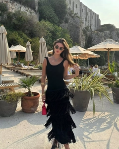 Détail de robe noire sans manches à franges avec sac à main rouge et bracelets dorés