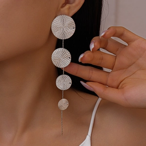 Détail de boucles d'oreilles argentées à pompons longs avec disques métalliques
