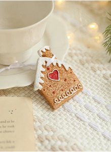 Close-up of a gingerbread house Christmas ornament with red accents on a cozy knit surface